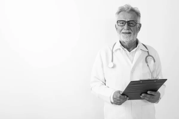 Студійний знімок щасливого старшого бородатого лікаря, посміхаючись, тримаючи кишеню на білому тлі — стокове фото