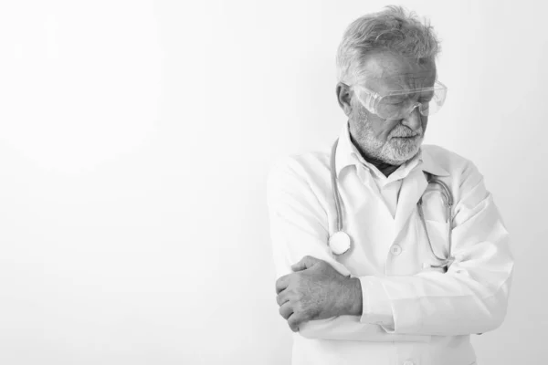 Studio colpo di triste anziano barbuto uomo medico pensando mentre indossa occhiali protettivi con le braccia incrociate sullo sfondo bianco — Foto Stock