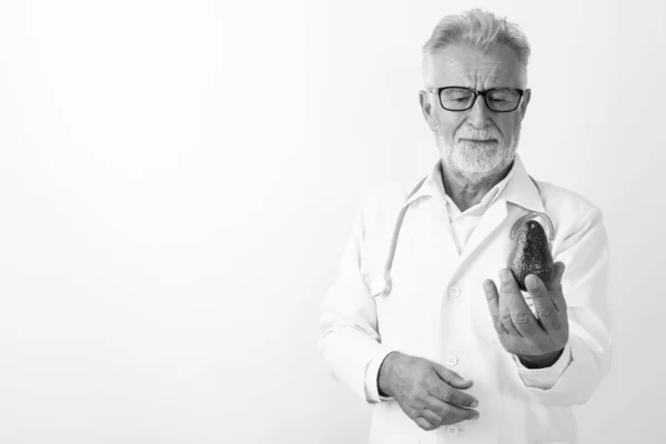 Studio colpo di bello anziano barbuto uomo medico guardando avocado contro sfondo bianco — Foto Stock