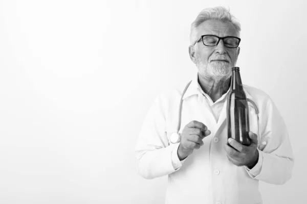 Studio záběr pohledný senior vousatý muž lékař čichání láhev piva se zavřenýma očima na bílém pozadí — Stock fotografie