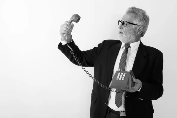 Profilo vista di arrabbiato senior barbuto uomo d'affari in possesso e guardando il vecchio telefono sullo sfondo bianco — Foto Stock