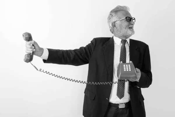 Estudio de tiro de hombre de negocios barbudo alto guapo sosteniendo el teléfono viejo mientras que mira molesto contra fondo blanco — Foto de Stock