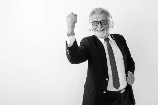 Studio colpo di felice anziano barbuto uomo d'affari sorridente durante l'ascolto di musica e guardando motivato con occhiali su sfondo bianco — Foto Stock