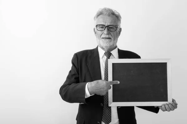 Studio shot van knappe senior bebaarde zakenman wijzend op blanco schoolbord tegen witte achtergrond — Stockfoto