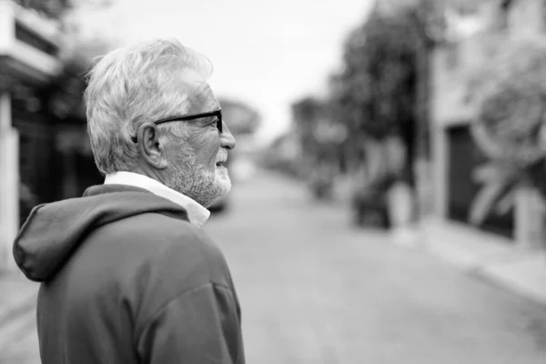 Profilbild av glad stilig seniorskäggig man som ler medan han bär glasögon utomhus — Stockfoto