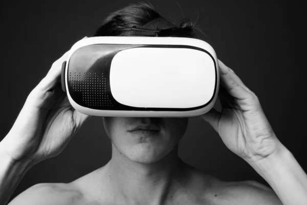 Jovem homem bonito usando óculos de realidade virtual sem camisa contra fundo cinza — Fotografia de Stock