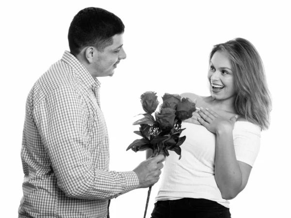 Joven pareja feliz sonriendo y enamorada de hombre dando rosas y mujer buscando sorprendida — Foto de Stock