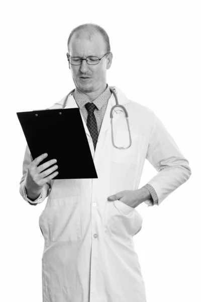 クリップボードを読んでいる間に立っている男医師のスタジオショット — ストック写真