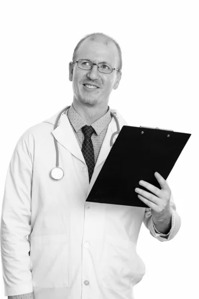 Studio shot of happy man médecin souriant tout en tenant presse-papiers et la pensée — Photo