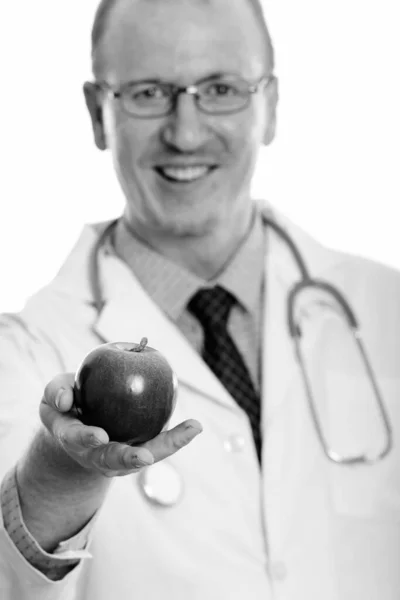Студійний знімок щасливого лікаря, який посміхається, даючи яблуко з фокусом на яблуці — стокове фото