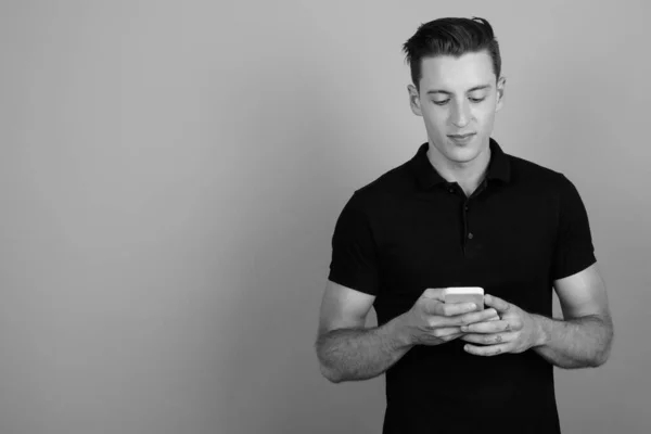 Νεαρός όμορφος άντρας που χρησιμοποιεί κινητό τηλέφωνο σε γκρι φόντο — Φωτογραφία Αρχείου