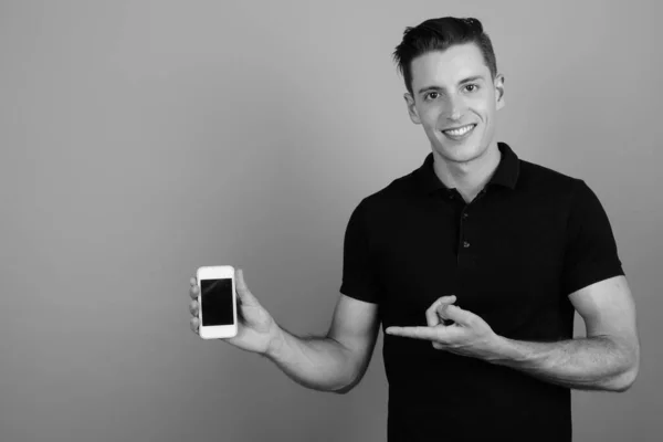 Jeune homme beau en utilisant un téléphone mobile sur fond gris — Photo