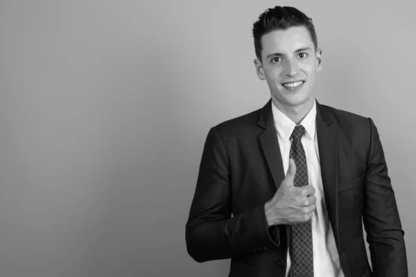 Jonge knappe zakenman draagt pak tegen grijze achtergrond — Stockfoto