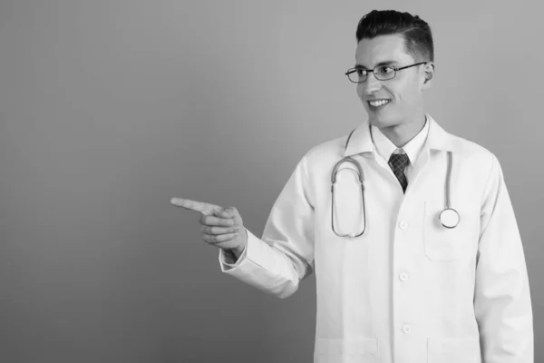 Junger schöner Mann Arzt vor grauem Hintergrund — Stockfoto