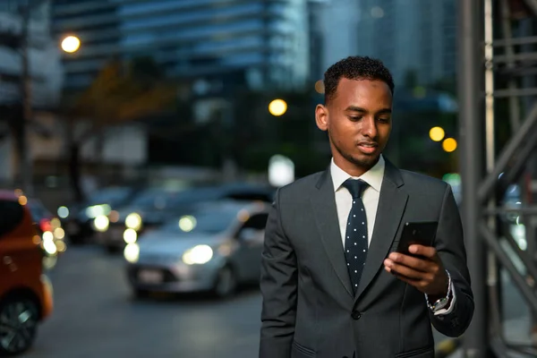 Empresário africano ao ar livre à noite usando telefone celular — Fotografia de Stock