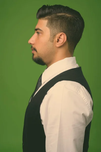 Young bearded Iranian businessman against green background