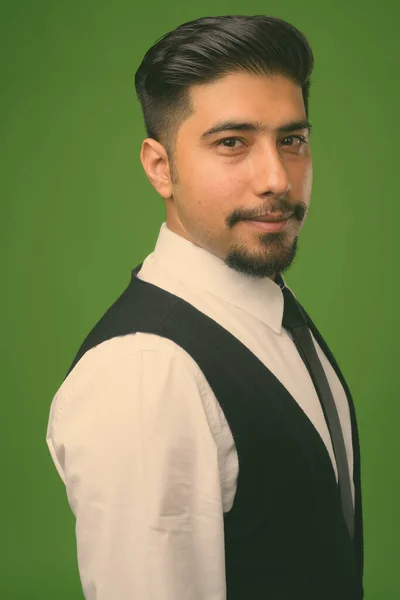 Young bearded Iranian businessman against green background