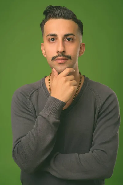 Jonge knappe Iraanse man met snor tegen groene achtergrond — Stockfoto