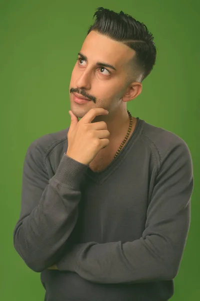 Young handsome Iranian man with mustache against green background