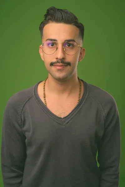 Young handsome Iranian man with mustache against green background