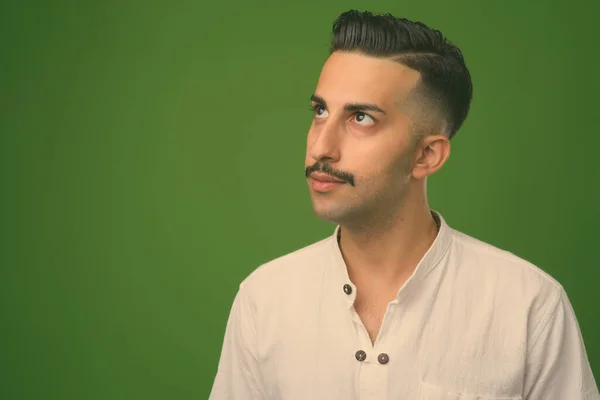 Young handsome Iranian man with mustache against green background