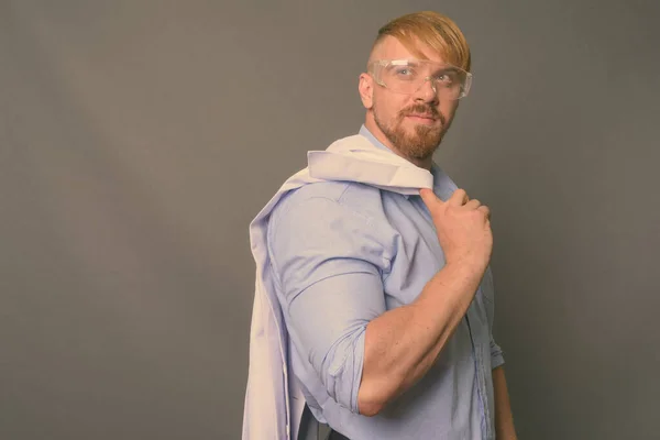 Hombre barbudo doctor con cabello rubio usando gafas protectoras contra fondo gris —  Fotos de Stock