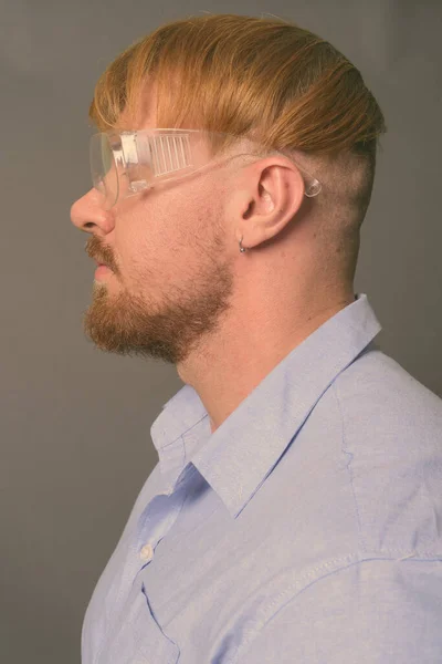 Hombre barbudo doctor con cabello rubio usando gafas protectoras contra fondo gris —  Fotos de Stock