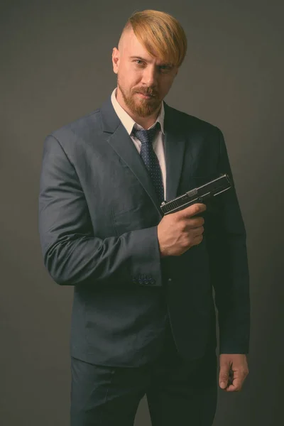 Bearded businessman with handgun against gray background — Stock Photo, Image