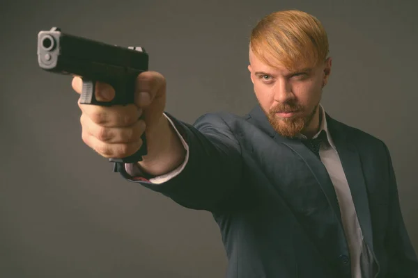 Empresario barbudo con pistola contra fondo gris —  Fotos de Stock