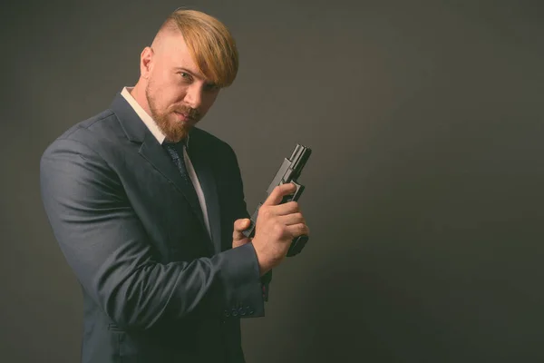 Empresario barbudo con pistola contra fondo gris —  Fotos de Stock