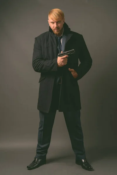 Uomo d'affari barbuto con pistola contro sfondo grigio — Foto Stock