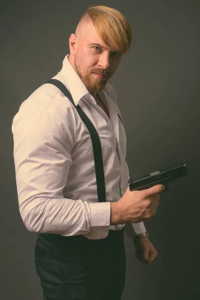 Бородатый мужчина с пистолетом на сером фоне — стоковое фото