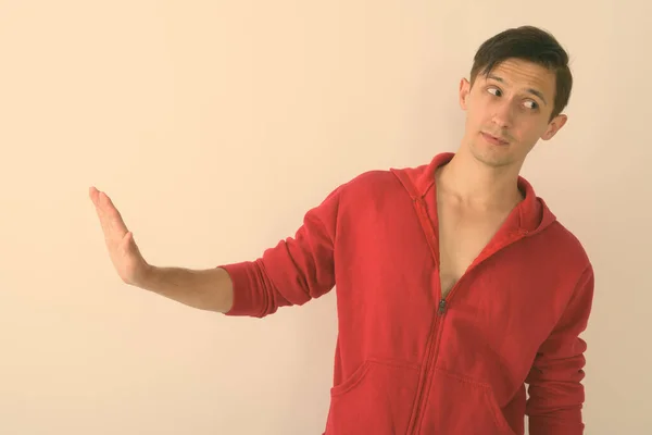 Studio shot of young handsome man thinking while showing stop hand sign to the side against white background — Stock Photo, Image