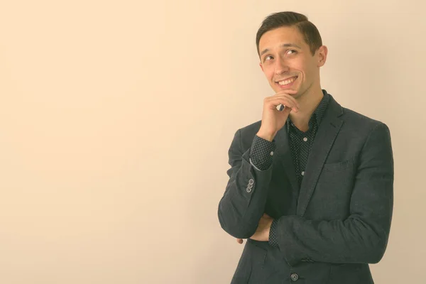 Estúdio tiro de jovem empresário feliz sorrindo e pensando ao olhar para cima contra fundo branco — Fotografia de Stock