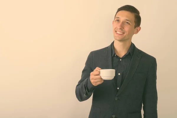 Studio colpo di giovane uomo d'affari felice sorridente e pensando, mentre tenendo tazza di caffè sullo sfondo bianco — Foto Stock
