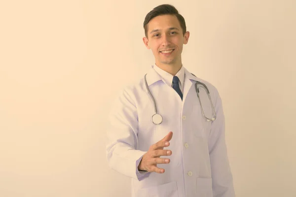 Estudio de tiro de joven feliz hombre médico sonriendo mientras que da apretón de manos sobre fondo blanco —  Fotos de Stock