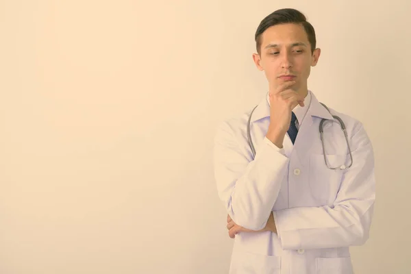 Estúdio tiro de jovem bonito homem médico pensando enquanto olha para baixo contra fundo branco — Fotografia de Stock