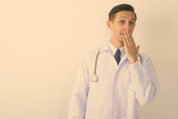 Stúdió lövés fiatal jóképű férfi orvos fedő száj kézzel ellen fehér háttér — Stock Fotó