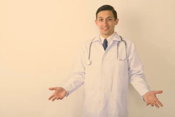 Studio záběr mladý šťastný muž lékař usmívá při pohledu zmatený proti bílému pozadí — Stock fotografie