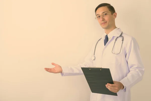 Στούντιο πλάνο του νεαρού όμορφος γιατρός άνθρωπος δείχνει κάτι και κρατώντας πρόχειρο φορώντας γυαλιά ηλίου σε λευκό φόντο — Φωτογραφία Αρχείου