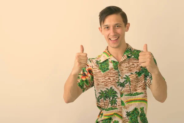 Studio shot of young happy tourist man smiling while giving thumbs up against white background — Stock Photo, Image