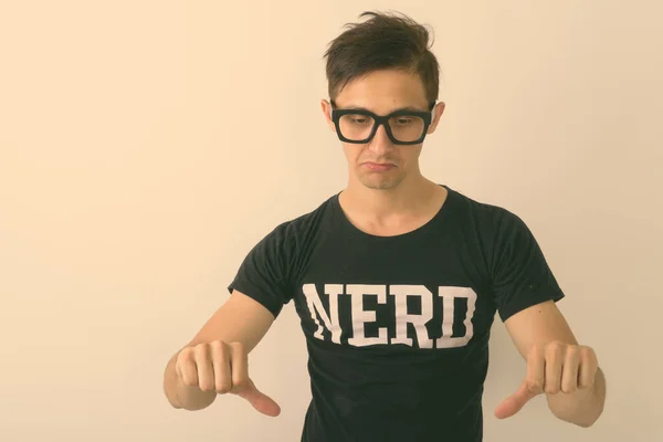 Estudio de tiro de joven nerd hombre mirando triste y dando pulgares hacia abajo mientras llevaba gafas sobre fondo blanco — Foto de Stock