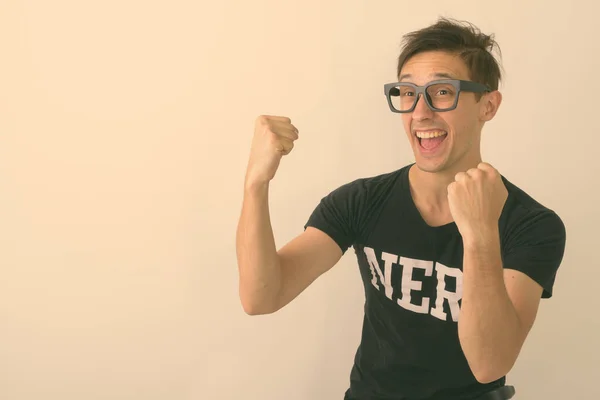 Estúdio tiro de jovem feliz nerd homem sorrindo ao pensar e olhando animado contra fundo branco — Fotografia de Stock