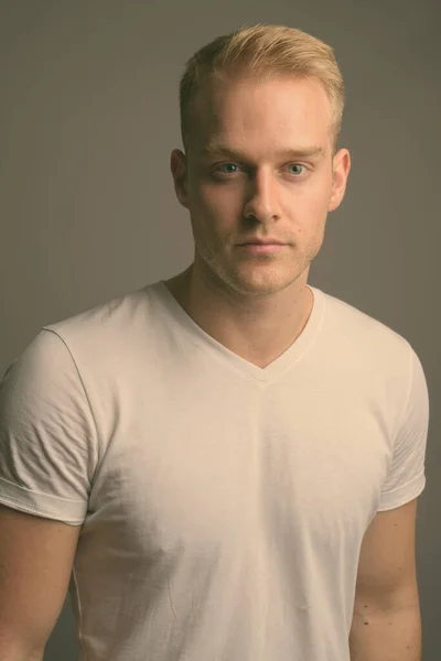 Young handsome man with blond hair against gray background