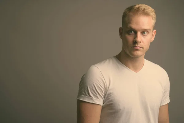 Young handsome man with blond hair against gray background