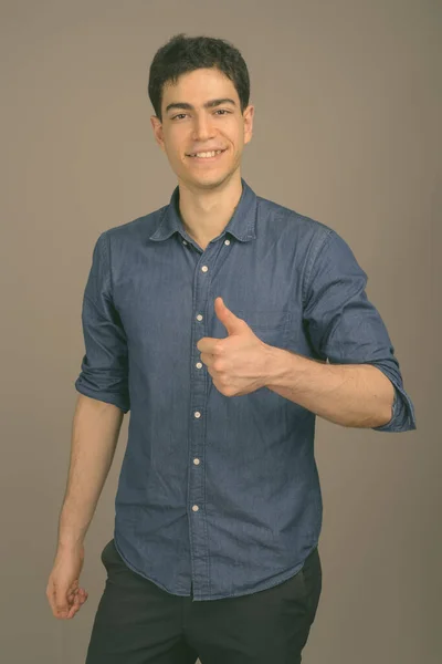 Portrait of happy young handsome businessman against gray background — Stock Photo, Image