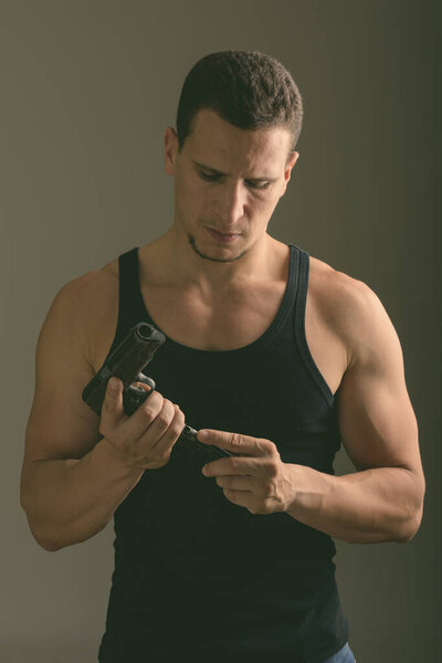 Студийный снимок молодого мускулистого перса, перезаряжающего пистолет в темной комнате