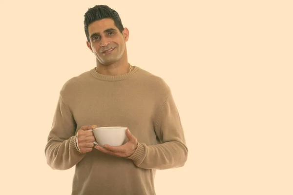 Estudio disparo de joven feliz musculoso persa hombre sonriendo mientras sostiene la taza de café —  Fotos de Stock