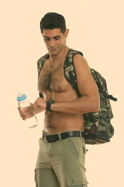 스튜디오에서 시계를 보면서 셔츠를 입지 않은 시간을 확인하는 동안 물병을 든 젊은 근육질의 페르시아 남자의 사진을 찍었다 — 스톡 사진