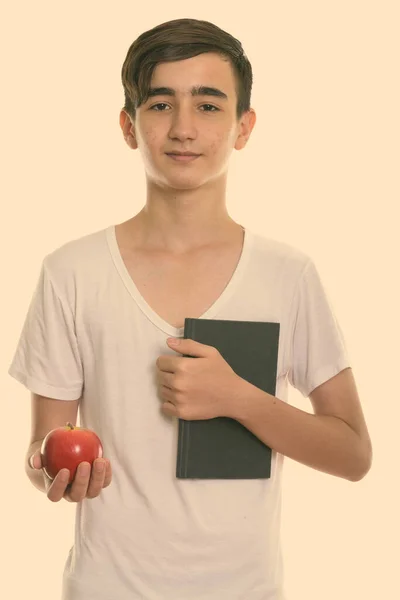 Studio shot de jeune adolescent persan beau tenant livre et pomme rouge — Photo